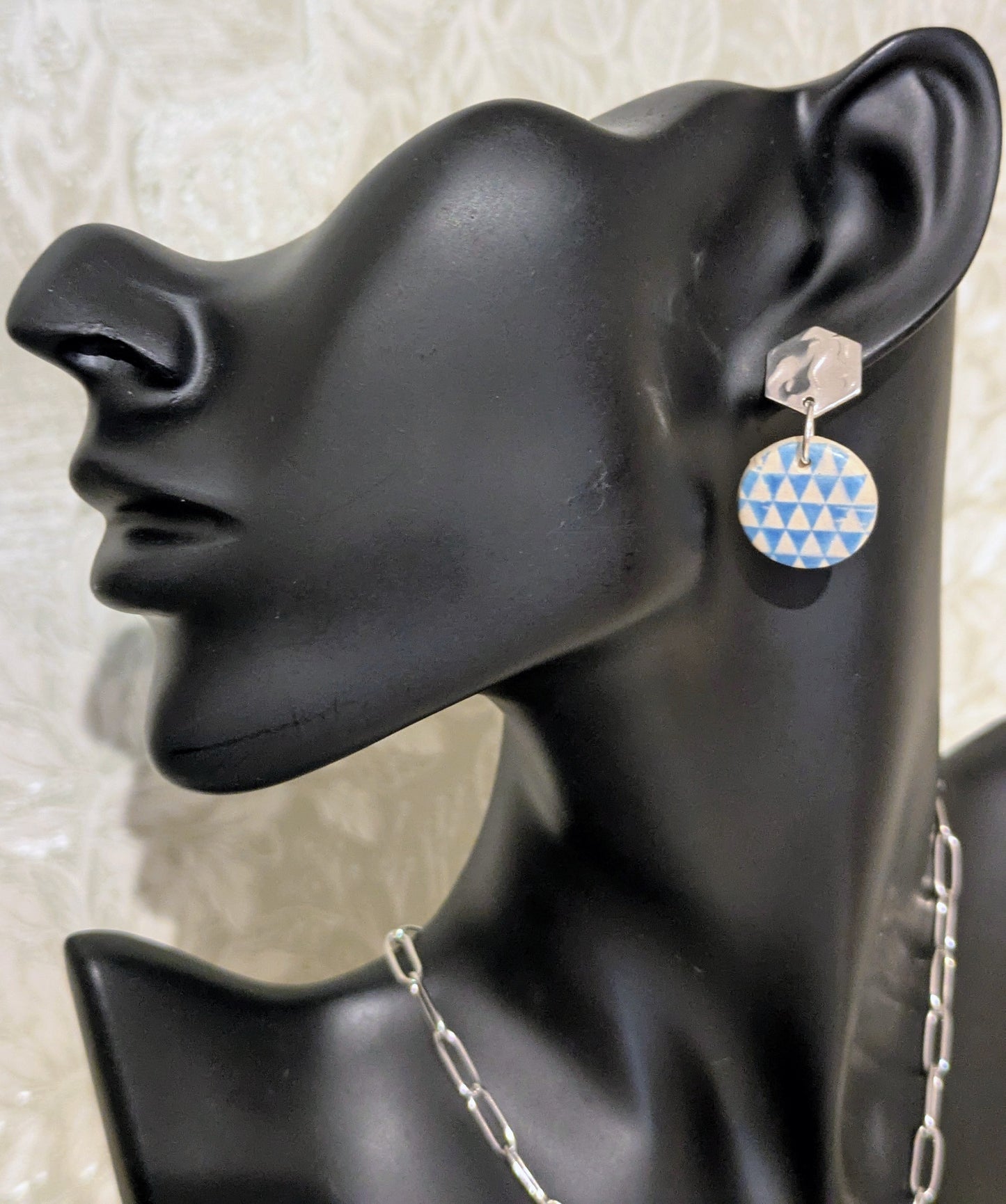 Earring displayed on a black mannequin ear with a geometric patterned earring.